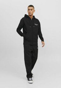 Zwarte rits hoodie van katoenmix, met een trekkoordkapuchon en voorzakken. Gecombineerd met bijpassende zwarte sweatpants en sneakers.