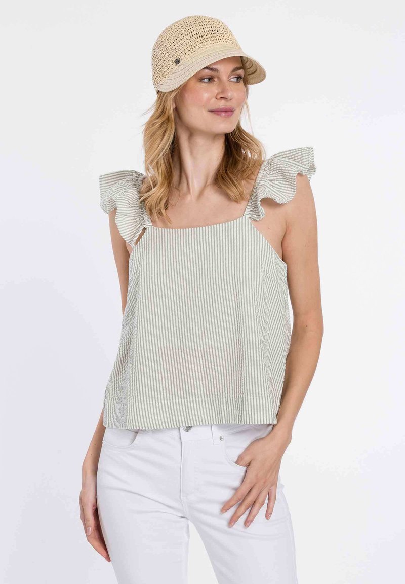 Top sin mangas a rayas con acentos de hombros volantes, en colores verde claro y blanco. Combinado con pantalones blancos. Lleva una gorra de paja beige.