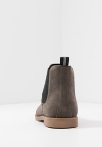 Szare zamszowe botki Chelsea z czarnymi elastycznymi panelami bocznymi i niską brązową gumową podeszwą. Posiadają małą pętelkę z tyłu ułatwiającą zakładanie.