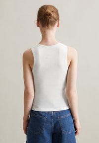 Witte geribbelde tanktop met een ronde hals en zonder mouwen, gecombineerd met hoge blauwe denim shorts met twee achterzakken.