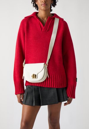 Maglione rosso lavorato a maglia con colletto polo, abbinato a una borsa a tracolla in pelle bianca con chiusura dorata e un design strutturato. Gonna a quadri nera.