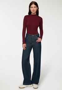 Body a maniche lunghe bordeaux abbinato a jeans scuri a gamba larga e vita alta. Caratteristiche includono una silhouette aderente e dettagli di cucitura sottili.