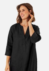 Schwarzes Leinen-Tunikakleid mit Dreiviertelärmeln, V-Ausschnitt und lockerer Passform. Weicher Stoff, minimalistische Details und klassisches Design.