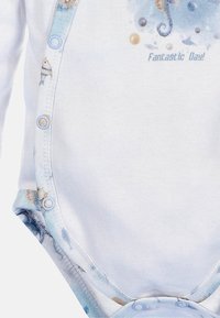 Witte katoenen romper met lichtblauwe randen en vissenpatroon, drukknoopsluiting aan de onderkant en de tekst "Fantastische Dag!" in lichtblauw.