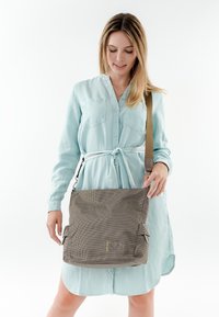 Borsa a spalla grigia con texture, dotata di tracolla regolabile e tasche esterne. La borsa presenta un logo discreto nella parte anteriore. Tessuto morbido, forma rettangolare.
