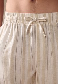 Pantalon en lin à rayures verticales beige et blanches, doté d'une taille élastique avec cordon de serrage. Texture douce et coupe légère.