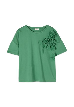 Camicia verde a maniche corte con scollo rotondo, caratterizzata da applicazioni floreali in rilievo raggruppate nella parte superiore sinistra del petto e nella zona della spalla.