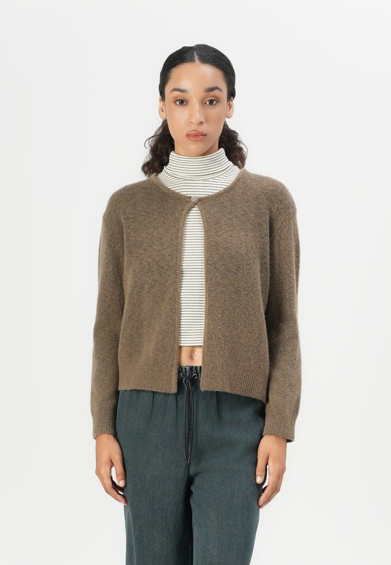 Brown knitted cardigan with a round neckline, open front, and no buttons. Worn over a striped turtleneck, with long sleeves and a cropped design.