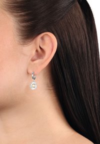 Pendientes de aro de plata con un colgante redondo que presenta un diseño floral texturizado y una piedra preciosa clara en el centro.