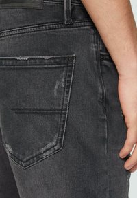 Czarne dżinsy o zniszczonym wyglądzie, klasyczny pięcio-kieszeniowy fason oraz widoczna tylna kieszeń z subtelnym przetarciem.