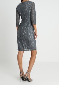 Robe en dentelle grise avec des manches trois-quarts, une coupe ajustée et un ourlet au genou. Portée avec des sandales à talons hauts argentées.