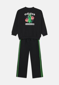 Schwarzer Sweatshirt mit einem Grafikdesign eines Minecraft Creepers und "adidas" Schriftzug; kombiniert mit schwarzen Hosen mit grünen Seitenstreifen.