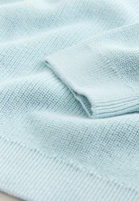 Világoskék kötött anyagú pulóver, texturált mintával, bordázott mandzsettákkal és sima öltésrészletekkel.