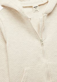 Sudadera blanca con textura, con cremallera y capucha, y bolsillos frontales. Cuenta con una cremallera suave y etiqueta de algodón, adecuada para niños de 4 a 5 años.