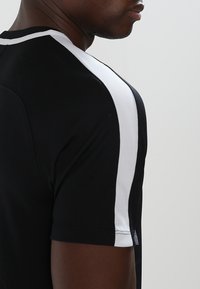 Czarna krótka koszulka sportowa z białymi akcentami na ramionach. Gładki materiał, dopasowany krój i zaokrąglony dekolt.