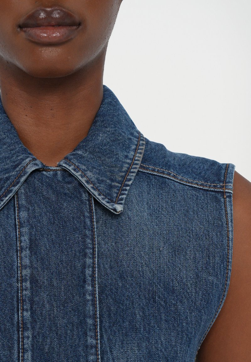 Ärmelloses Denim-Top mit klassischem Kragen, aus dunkelblauem Stoff, sichtbaren Nähten und einem verblassten Textur für einen Vintage-Look.