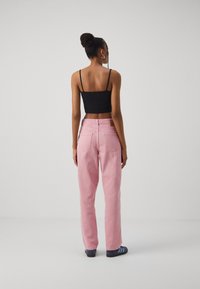 Ljusrosa jeans med lös passform och bakfickor, matchade med en svart kort topp och blårandiga sandaler, sedd bakifrån.