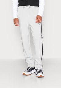 Ljusgrå sweatpants med svarta sidestreck, elastisk midja och dragsko. Tillsammans med svarta och vita sneakers med en kraftig sula.