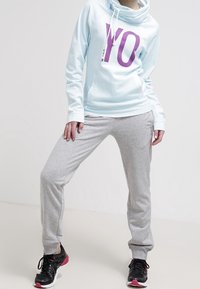 Sudadera azul claro con un gran gráfico púrpura de "YO", combinada con pantalones de chándal grises y zapatillas deportivas negras con acentos rosas.