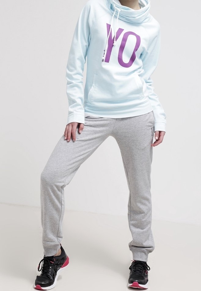 Sudadera azul claro con un gran gráfico púrpura de "YO", combinada con pantalones de chándal grises y zapatillas deportivas negras con acentos rosas.