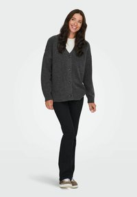Cardigan grigio carbone con scollatura a V, chiusura con bottoni e maniche lunghe. Abbinato a pantaloni neri e sneakers, con un tessuto testurizzato.