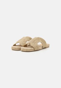 Naturlige fiber slip-on sandaler med et teksturert, vevd mønster i beige. Åpen tå-design med utskjærte accenter og en jute-såle.