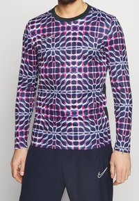 Dlouhý rukáv sportovní tričko s geometrickým vzorem v námořnické modři, růžové a bílé. Vyrobeno z elastického materiálu, má kulatý výstřih a přiléhavý střih.