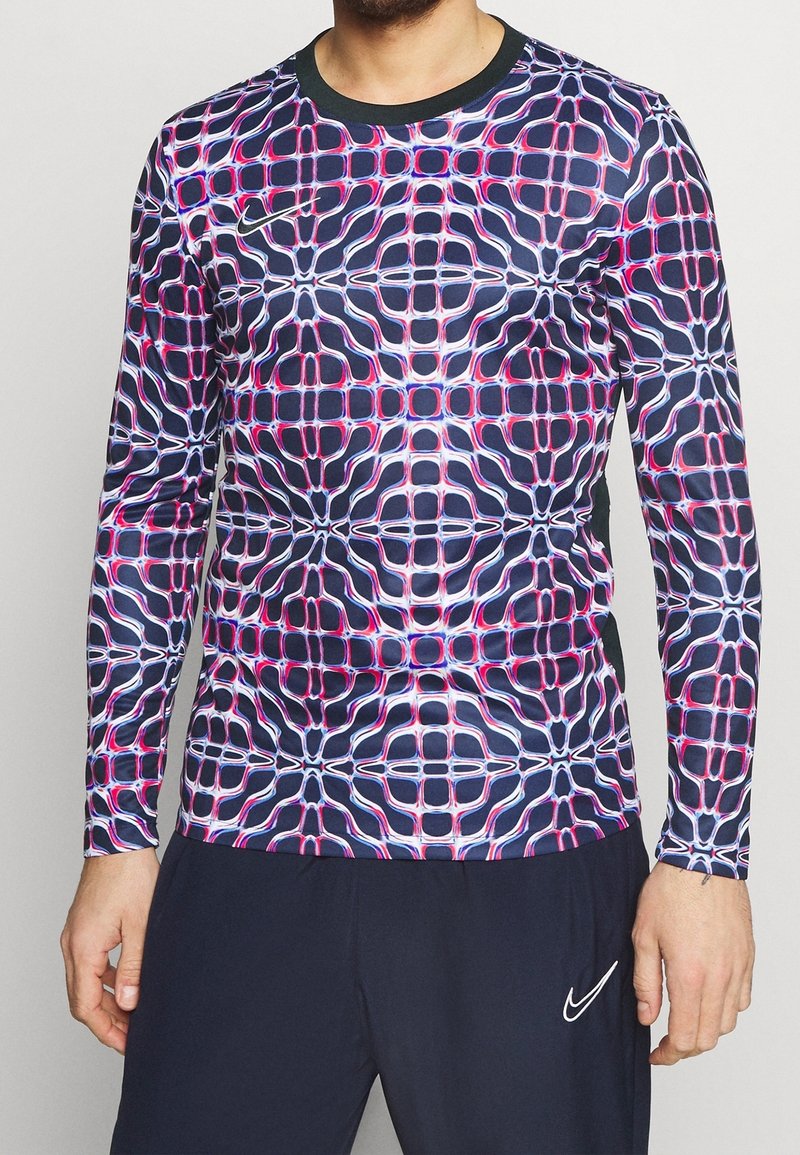 Dlouhý rukáv sportovní tričko s geometrickým vzorem v námořnické modři, růžové a bílé. Vyrobeno z elastického materiálu, má kulatý výstřih a přiléhavý střih.