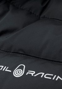 Svart vadderat tyg med en slät textur, med en vit "SAIL RACING"-logotyp. Designen inkluderar segmenterad sömnad för hållbarhet.