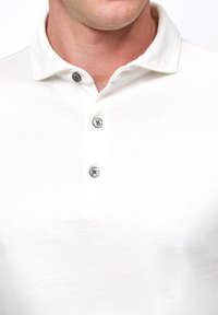 Weißes Polohemd mit einer weichen Textur, ausgestattet mit einem klassischen Kragen, drei metallischen Knöpfen und einer schlanken Passform.