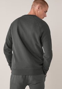 Tumehall kvaliteetne crewneck sviiter raglaanvarrukatega. Omab pehmet kangast, soonikkoeshari ja allserva. Tagantvaade näitab sileda tekstuuri ja sobivust.