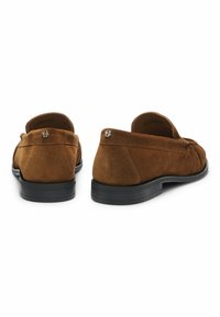 Καφέ σουέτ loafers με στρογγυλή μύτη, σχέδιο slip-on και μαύρη καουτσούκ σόλα. Περιέχει διακριτικές πτυχώσεις και μικρό λογότυπο στη φτέρνα.