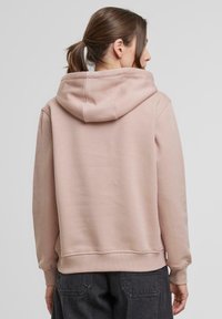 Ružová mikina s kapucňou, vo voľnom strihu, z mäkkého fleece materiálu, s rebrovanými manžetami a vreckom typu kengura na prednej strane.
