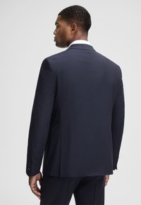 Navy strukturierte Anzugjacke mit einem dünnen Schlitz, zwei Knöpfen und einer taillierten Passform. Mit einem Kentkragen und schwarzen Knopfakzenten an den Ärmelbündchen.