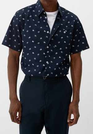 Camicetta navy a maniche corte con motivi floreali bianchi, design con bottoni, taschino sul petto e tessuto leggero. Abbinata a pantaloni scuri.
