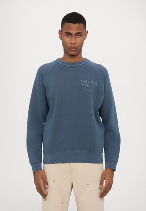 Blauwe katoenen sweatshirt met raglanmouwen, geribbelde halslijn en boorden, met de tekst "DAILY DOSE OF DENIM" op de borst.