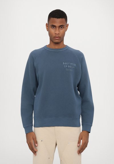 Felpa in cotone blu con maniche raglan, colletto e polsini a costine, caratterizzata dalla scritta "DOSE GIORNALIERA DI JEANS" sul petto.