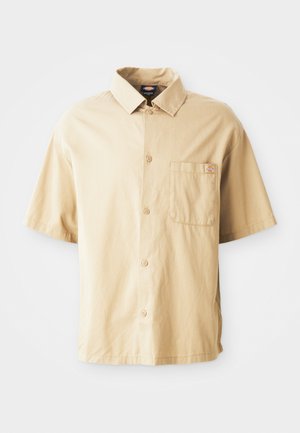 Beige kortärmad skjorta med spetsad krage, knappstängning fram, en bröstficka och en liten broderad logotyp på fickan.