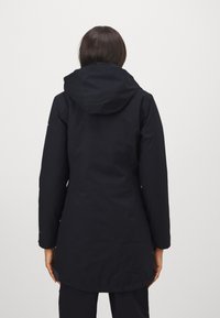 Svart vanntett jakke med hette, med lange ermer og middels lengde. Glatt tekstur med minimalistiske detaljer.
