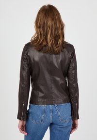 Braune Lederjacke mit taillierter Passform, Reißverschlussärmeln und glatter Textur. Dazu getragen werden blaue Jeans aus Denim mit detaillierten Nähten hinten.