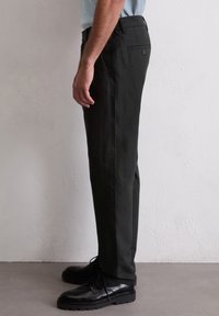 Dunkelgrüne, rechteckig geschnittene Hosen aus einer Baumwollmischung, mit seitlichen Taschen und einer knöpfbaren Gesäßtasche, glatter Textur und Gürtelschlaufen.