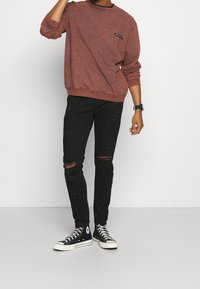 Rustinvärgad sweatshirt med rund halsringning och en liten lapplomme, ihop med svarta slitna slim-fit jeans och svarta hög-top sneakers.