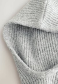 Tissu en tricot côtelé gris clair avec une texture douce, présentant un pli sur le bord, créant un aspect confortable et chaleureux.