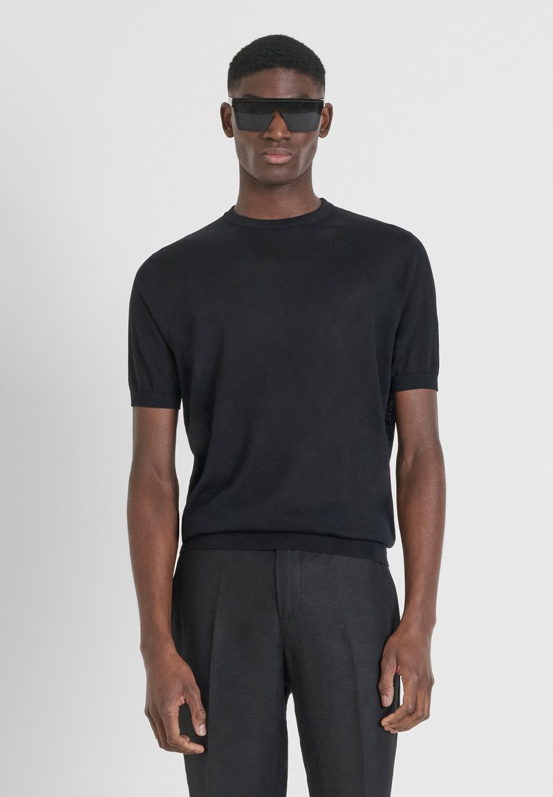 Maglione a maniche corte nero in maglia con scollatura rotonda, caratterizzato da una vestibilità slim e profili a costine, abbinato a pantaloni neri sartoriali.