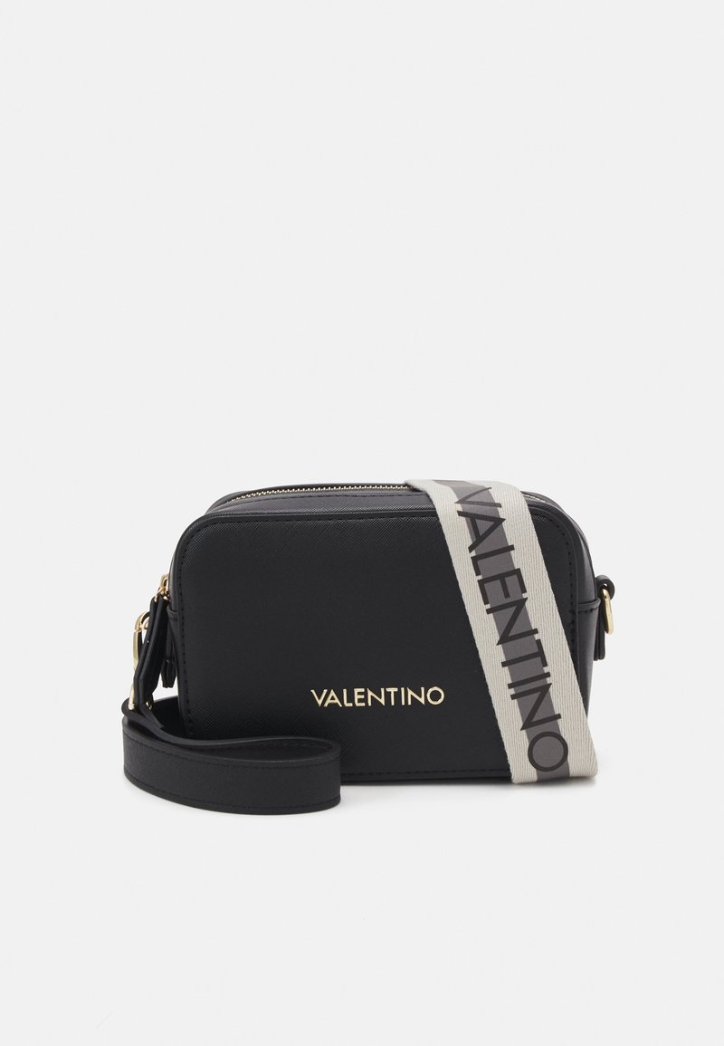 Sac en cuir noir à bandoulière avec un logo doré, doté d'une sangle beige contrastante avec le nom de la marque, fermeture zippée et forme rectangulaire.