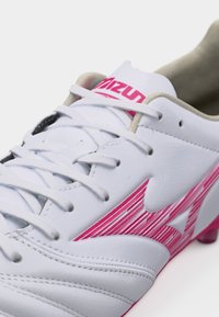 Λευκό ποδοσφαιρικό παπούτσι Mizuno με ροζ λογότυπο, δέσιμο κορδονιών και ορατές ραφές σε λευκό φόντο.