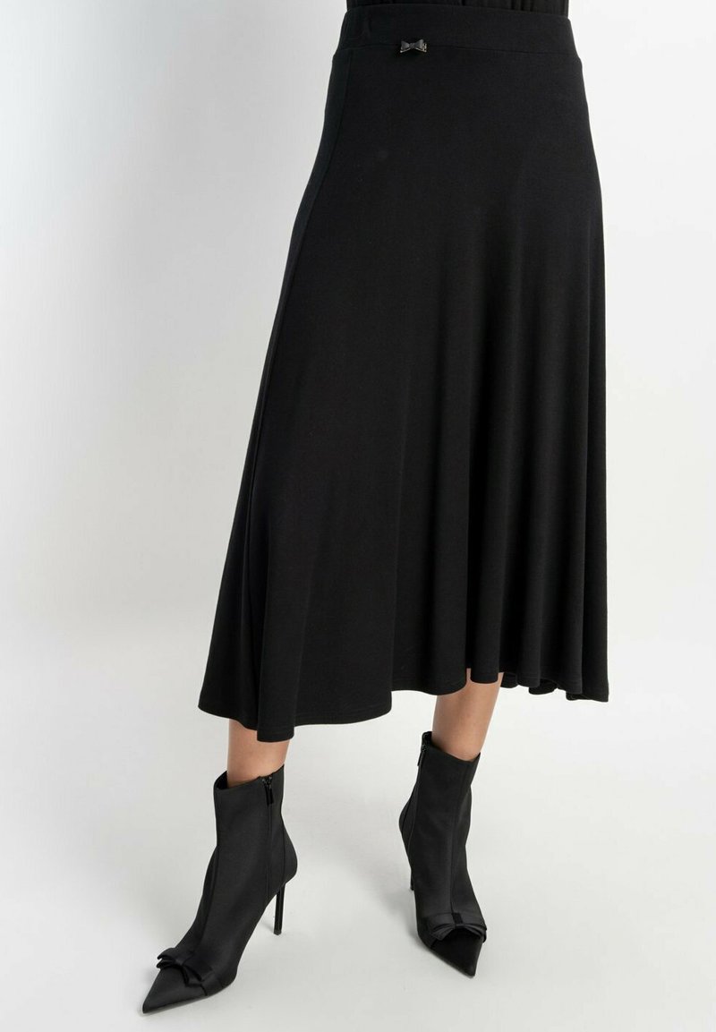 Czarna spódnica typu skater z miękkiego materiału, o gładkiej fakturze, z rozkloszowanym krojem i małą ozdobną kokardką w talii. Połączona z eleganckimi czarnymi botkami na kostkę.