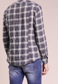 Szara i czarna koszula w kratę z długim rękawem cechuje się luźnym krojem, lekkim materiałem i guzikami na mankietach, w zestawie z niebieskimi dżinsami.