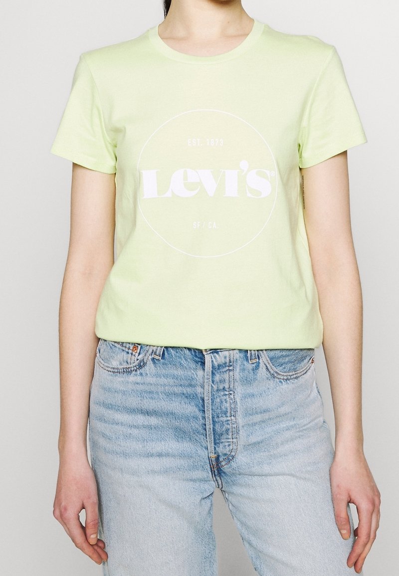 Camiseta de algodón verde claro con un logo circular blanco que incluye el texto "Levi's" y "EST. 1873", combinada con unos vaqueros de mezclilla azul claro.