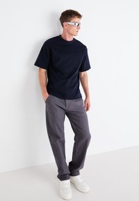 Marineblå kortermet t-skjorte, grå avslappede bukser, hvite joggesko og sølvfargede solbriller; minimalistisk design med en jevn tekstur.
